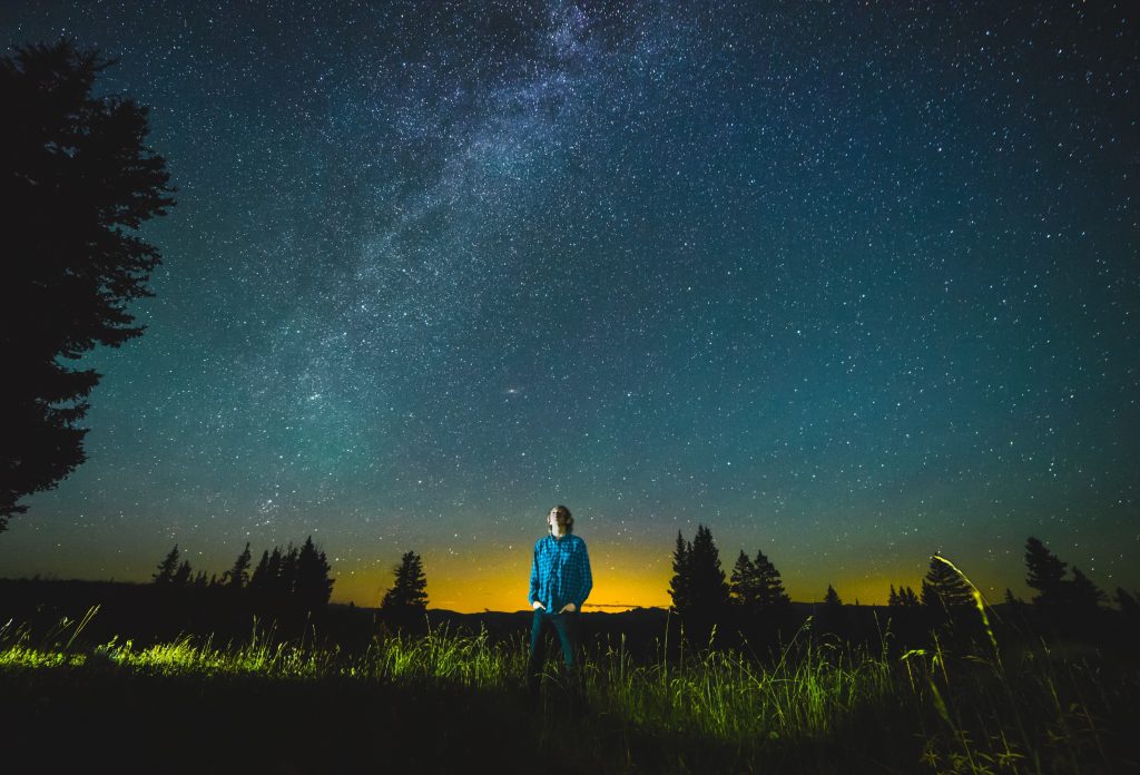 uma pessoa deslumbrada olhando o céu a noite. Comentários quanto as influências da Astronomia.