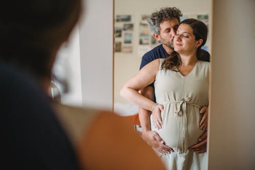 Um casal se abraçando e a esposa grávida foto tirada refletida do espelho. O Que é a Felicidade?