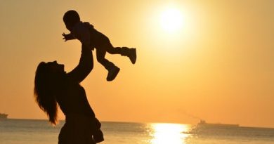 Uma mãe brincando com seu filho o elevando no alto e uma linda imagem do por do sol ao fundo. Homenagem ao dia das Mães