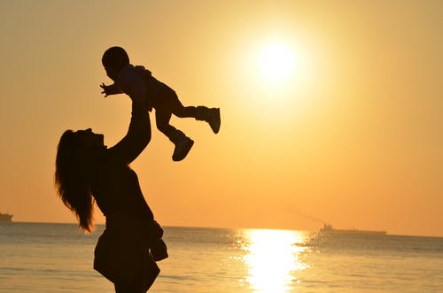 Uma mãe brincando com seu filho o elevando no alto e uma linda imagem do por do sol ao fundo. Homenagem ao dia das Mães