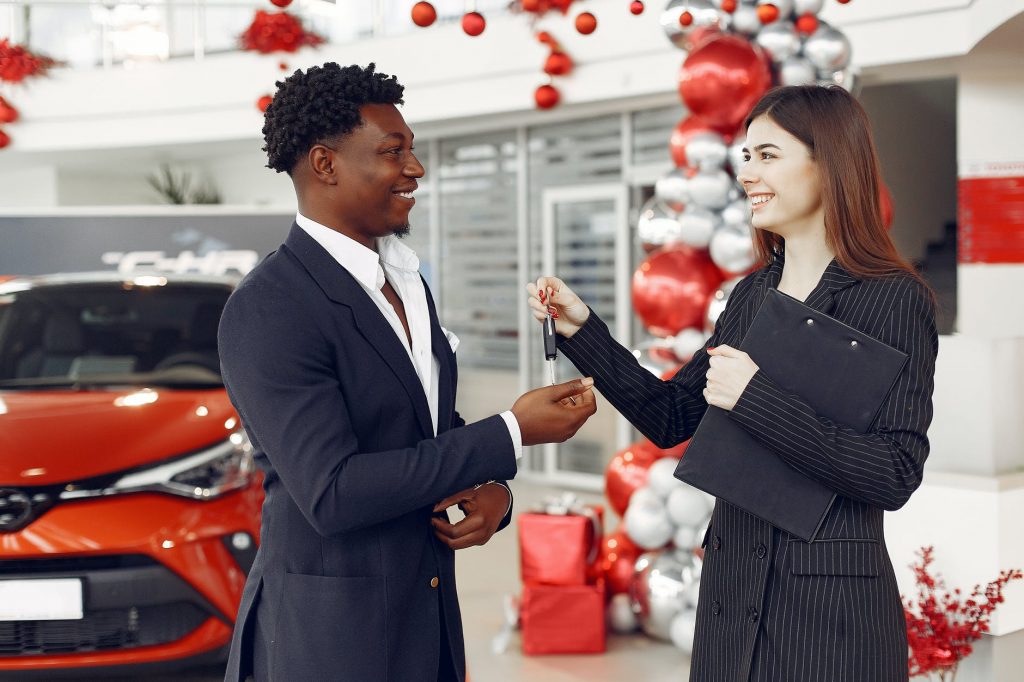 Uma vendedora entrega a chave de um carro ao seu cliente com sorriso no rosto. O que é preciso para ser um bom Vendedor(a), um Vendedor de Sucesso?