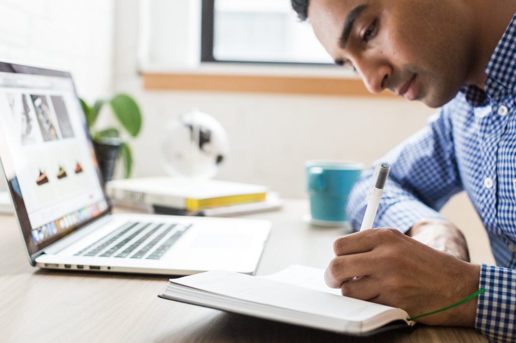 Uma pessoa fazendo anotações em uma agenda, em uma linda mesa de trabalho. Tenha um Foco Inteligente e sua Liderança será Inteligente.