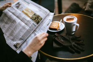 Uma pessoa lendo em uma mesa com um lindo cafezinho e torradas. 