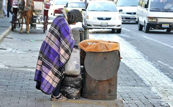 Uma pessoa maltrapilha pegando lixo em uma lata na rua. O Ser Humano e os sub-humanos ou “humanóides”