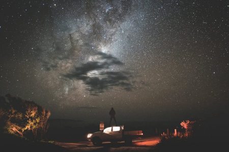 um homem encima de uma camionete olhando a imensidão do Cosmos. A Cosmologia e a Astronomia.