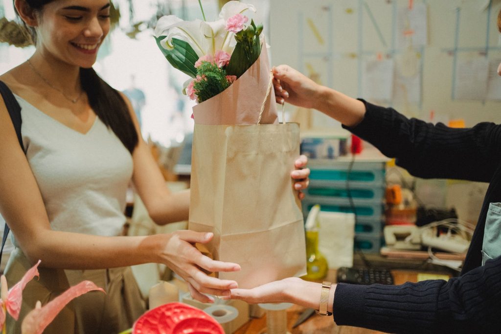 Atendente entregando uma bolsa com flores. Treinamento, Palestra ou Workshop – “Venda Mais com Qualidade: Foco no Atendimento ao Cliente”