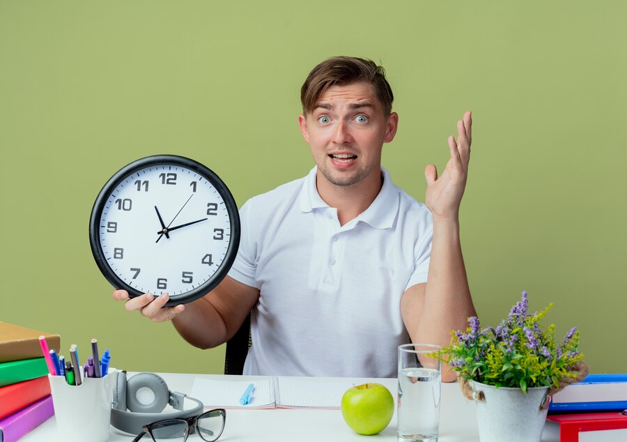 Um homem em usa mesa de trabalho com um relógio grande na mão marcando este tempo, como conseguir mais tempo?