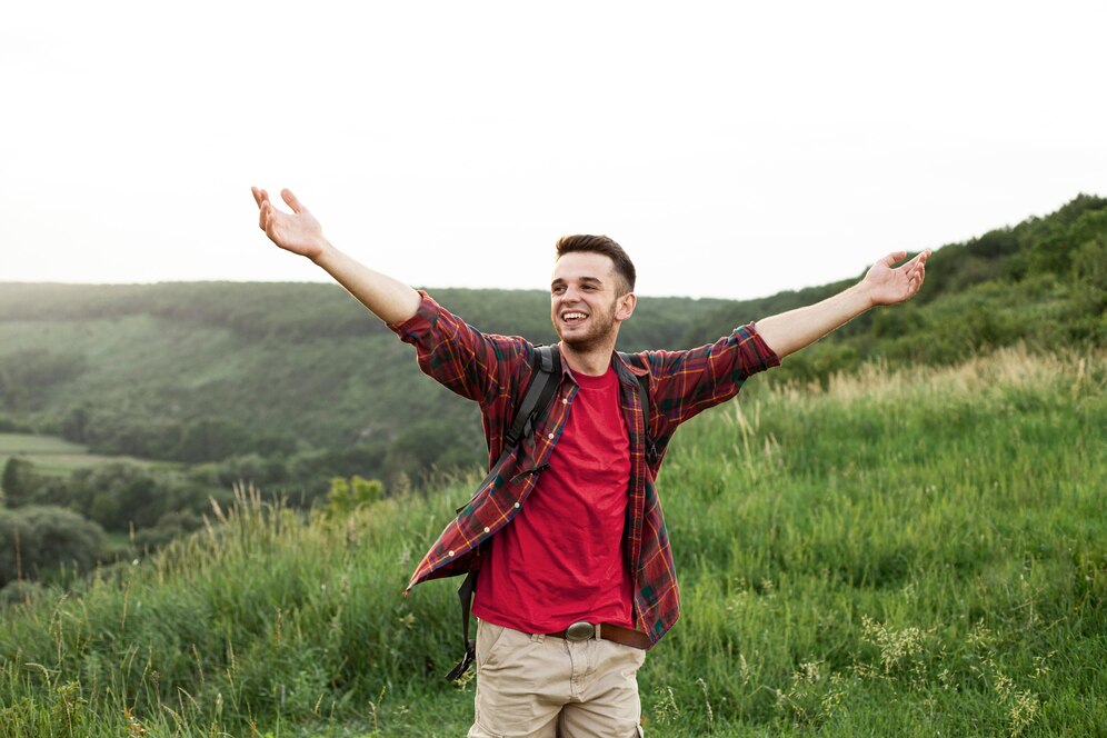 Homem de braços abertos aparenta felicidade em um lindo campo verde, quer ser feliz