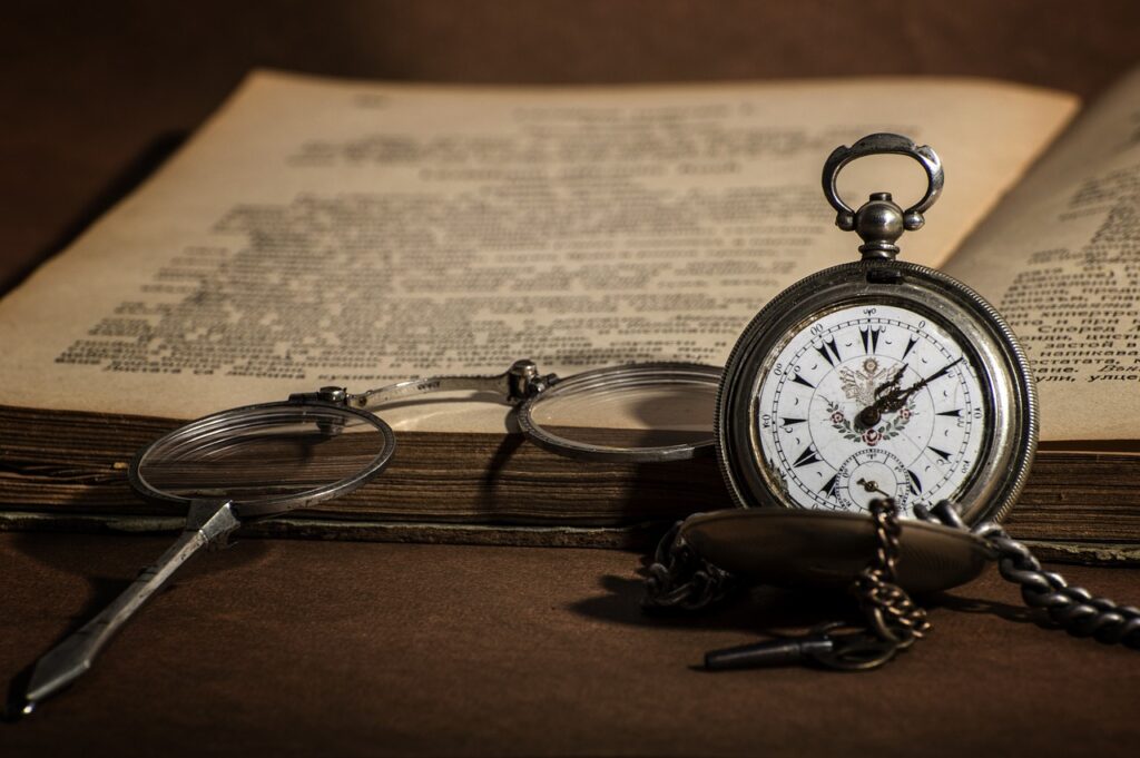 Em uma mesa se encontra um livro antigo e um relógio também antigo, ambos nos fazem pensar quanto a história do Conhecimento e como é complexo o conhecimento.